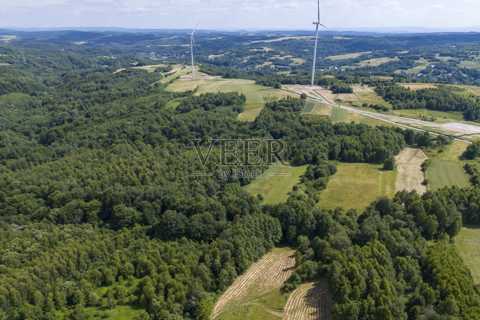 鸟瞰郁郁葱葱的绿田和森林，远处有风力发电机，展示可持续能源和自然风光照片摄影图片