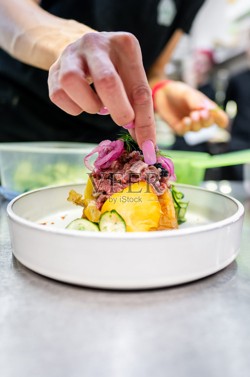 一只手在为色彩丰富的盘子装饰新鲜香草特写。菜肴呈现出鲜艳的绿色、黄色和红色元素，暗示着精致的美食展示。照片摄影图片