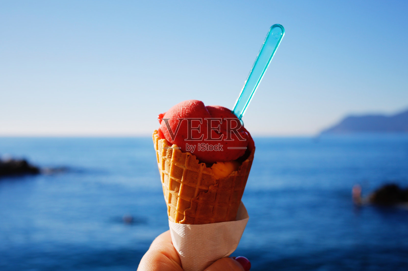 手握冰淇淋甜筒，背景是大海的特写镜头照片摄影图片