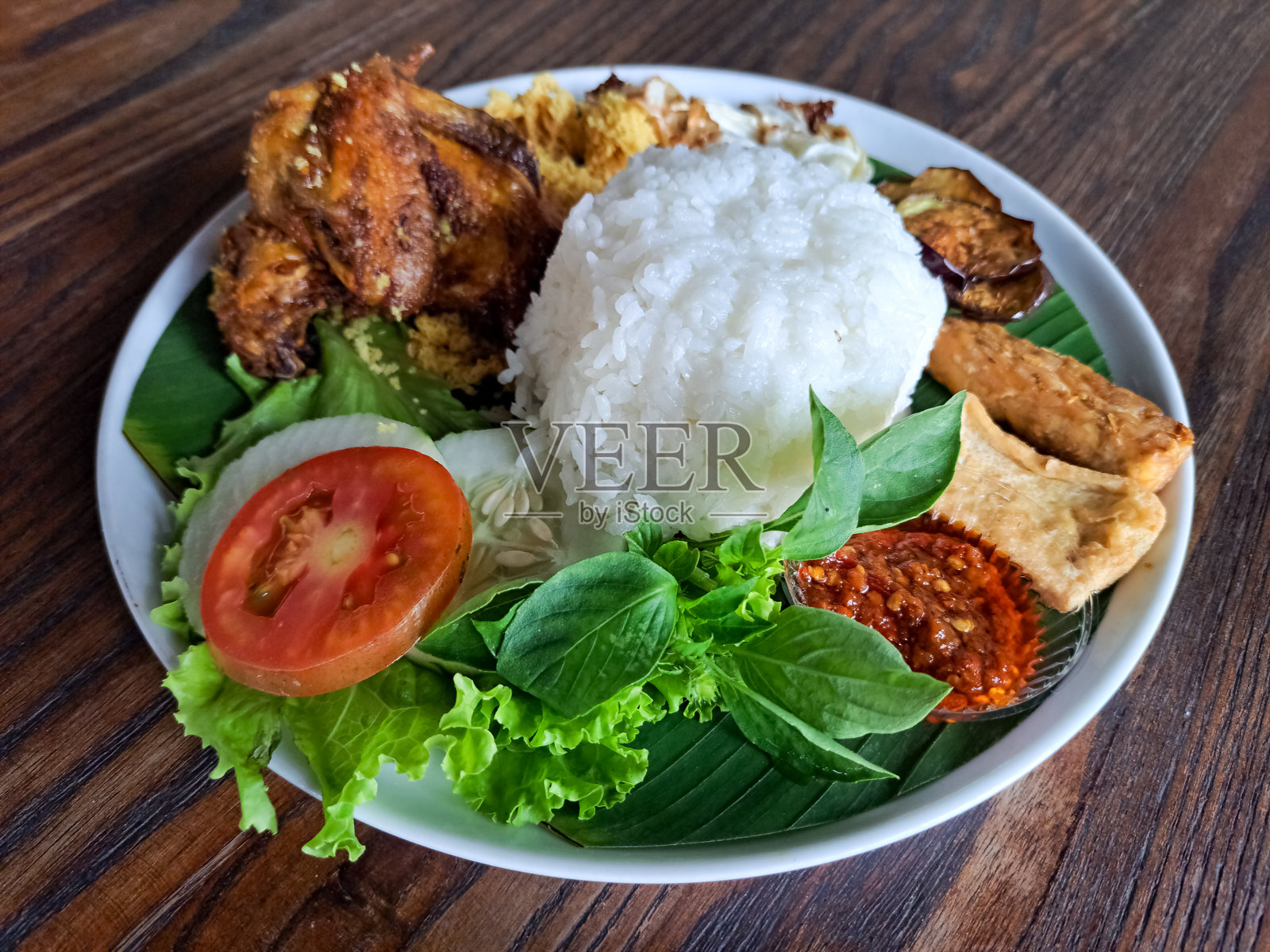 软骨炸鸡饭配香脆香料碎片、卷心菜、茄子、天贝、豆腐、辣椒酱、罗勒、黄瓜和西红柿。印尼美食菜单。照片摄影图片