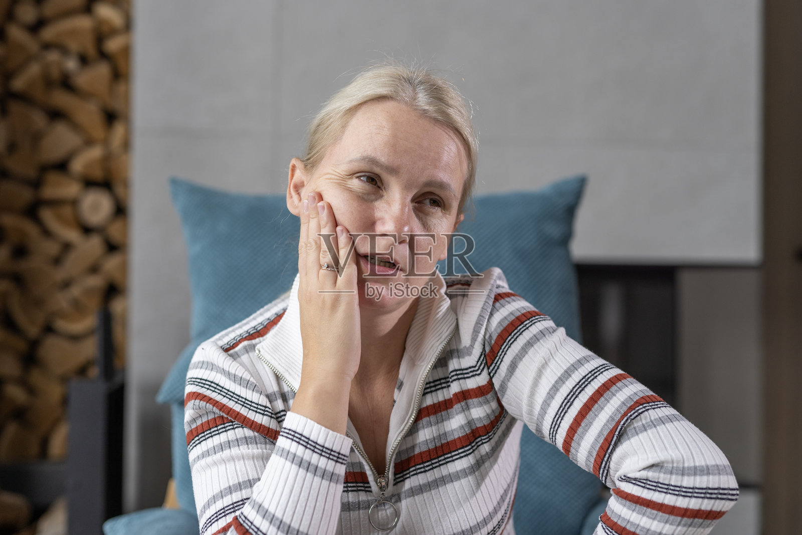 中年女性在舒适的家居环境中，面带沉思的表情，手托着脸颊。照片摄影图片