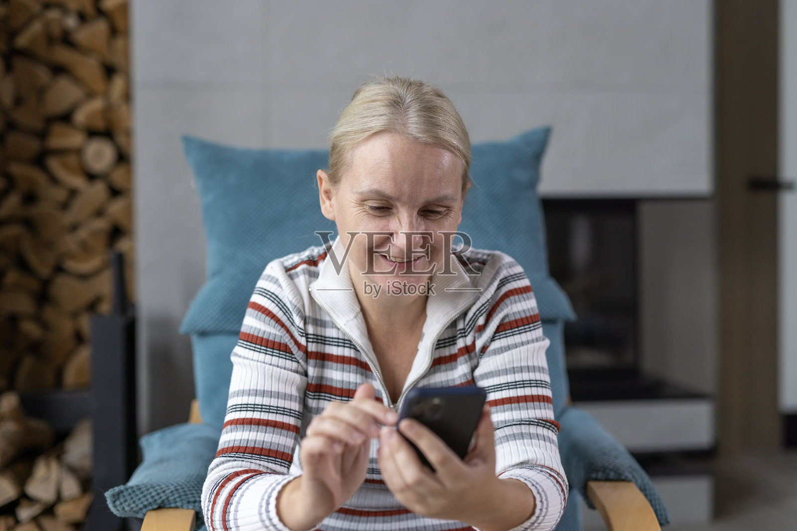 微笑的女性在室内使用智能手机，享受舒适环境中的轻松时刻。照片摄影图片