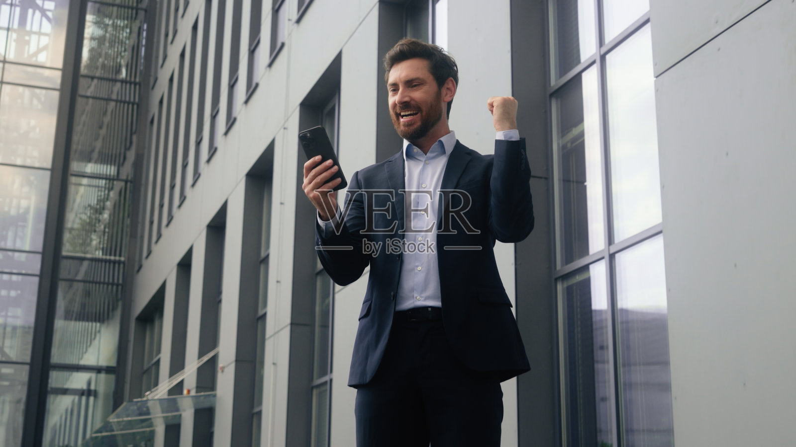 中年白人男性商人在市中心办公楼内，手持手机，庆祝成功，收到好消息，获得奖项。照片摄影图片