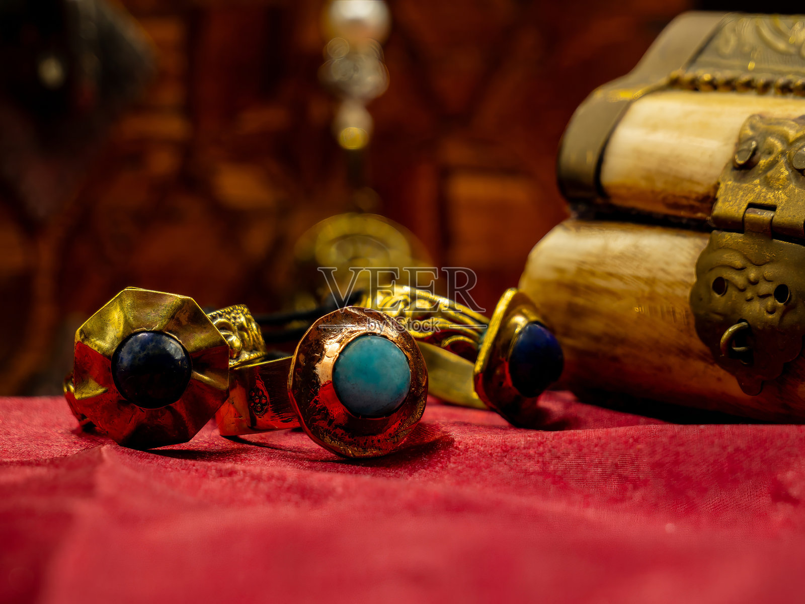 三枚装饰有宝石的中世纪戒指复制品，放置在红色天鹅绒背景和一个小箱子上。照片摄影图片