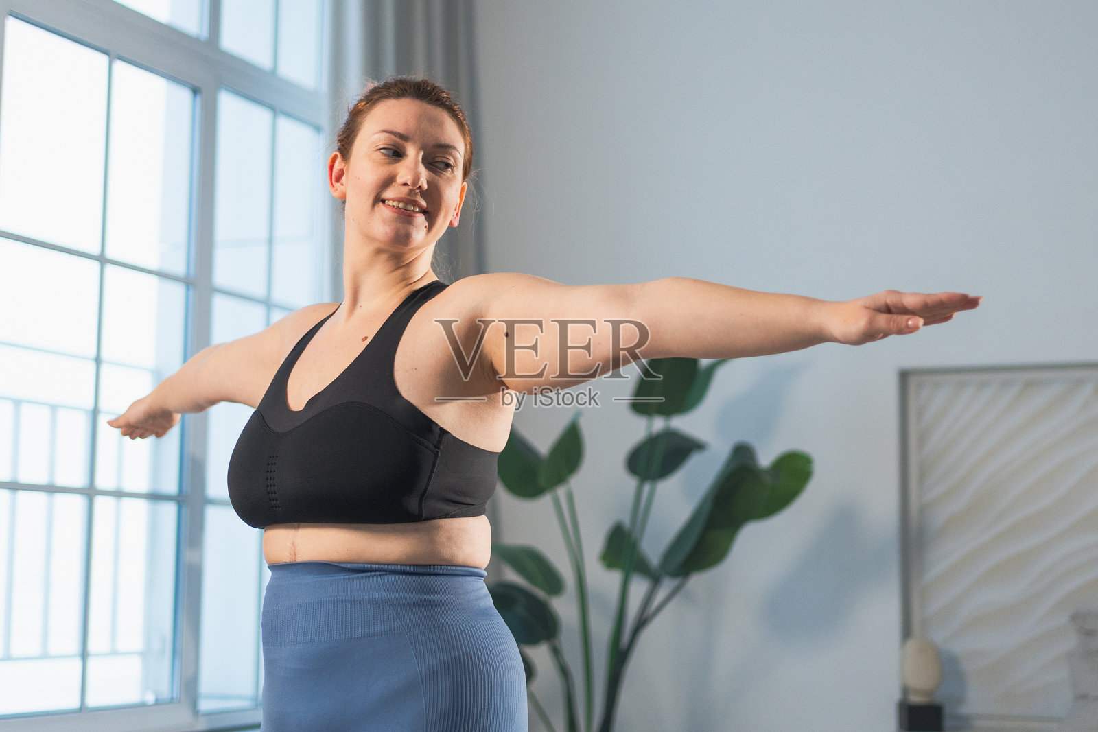 健身锻炼训练。女性在家中练习健身。加大码女性在室内进行运动锻炼。穿着运动服的女孩进行重量训练以减肥。运动与健身。照片摄影图片