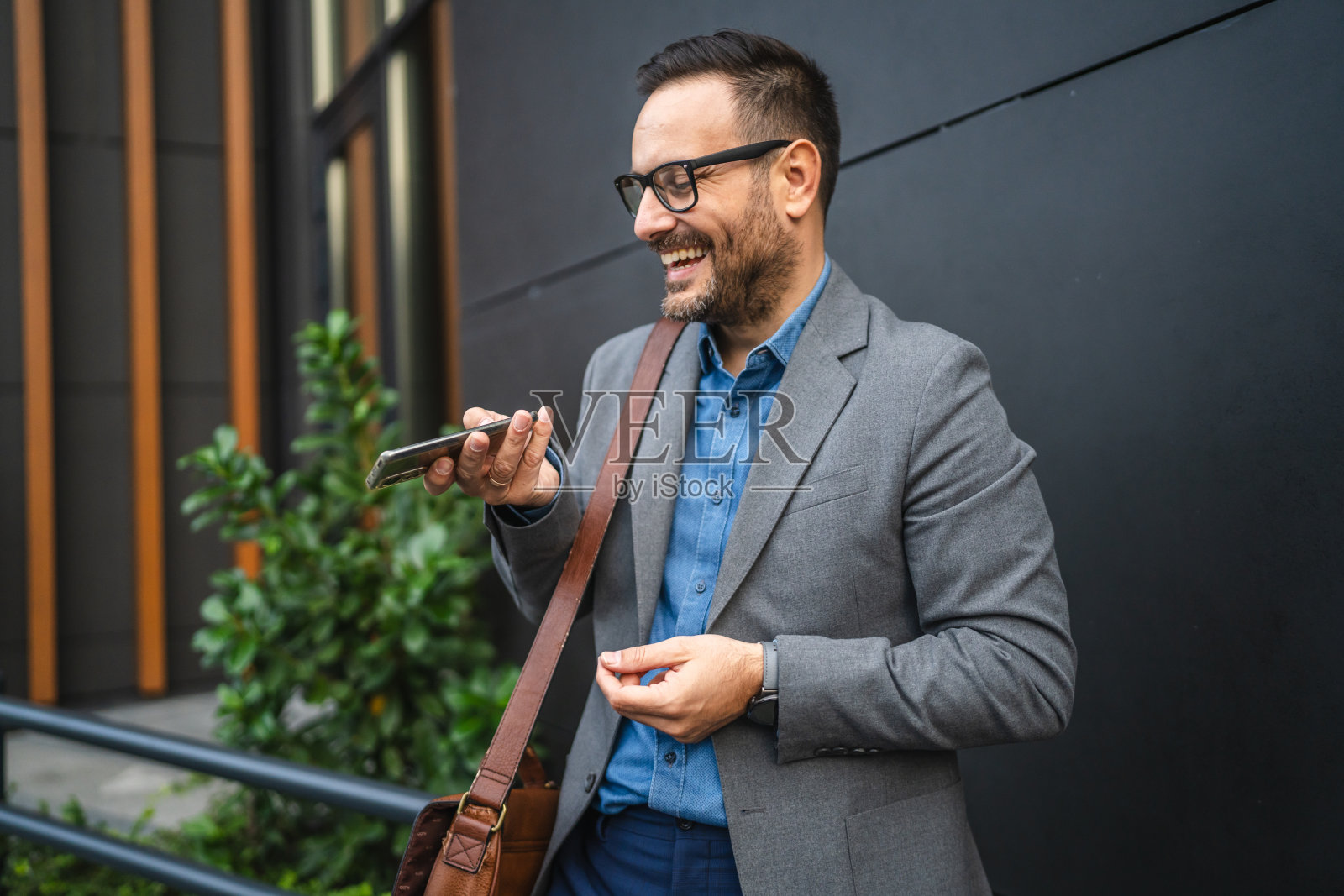 帅气的商人在黑色墙壁前站着，使用手机。照片摄影图片