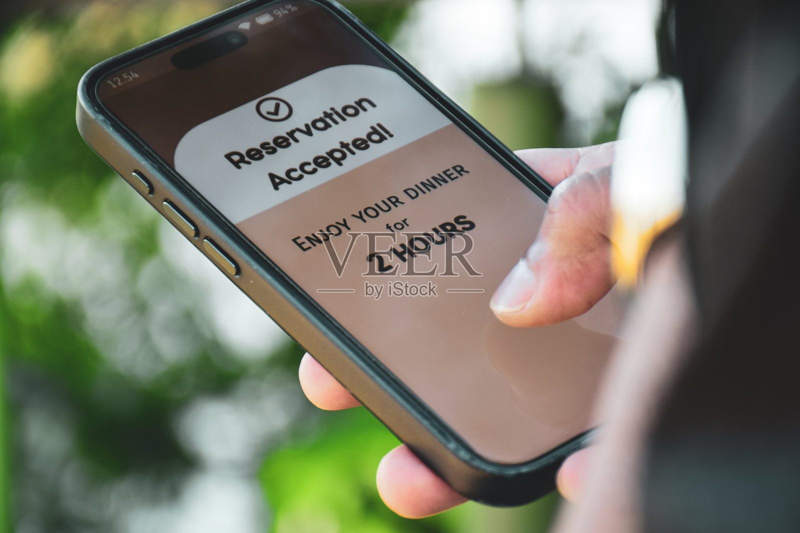 手机屏幕上的餐厅预订时间限制概念。特写镜头，手部在户外。照片摄影图片