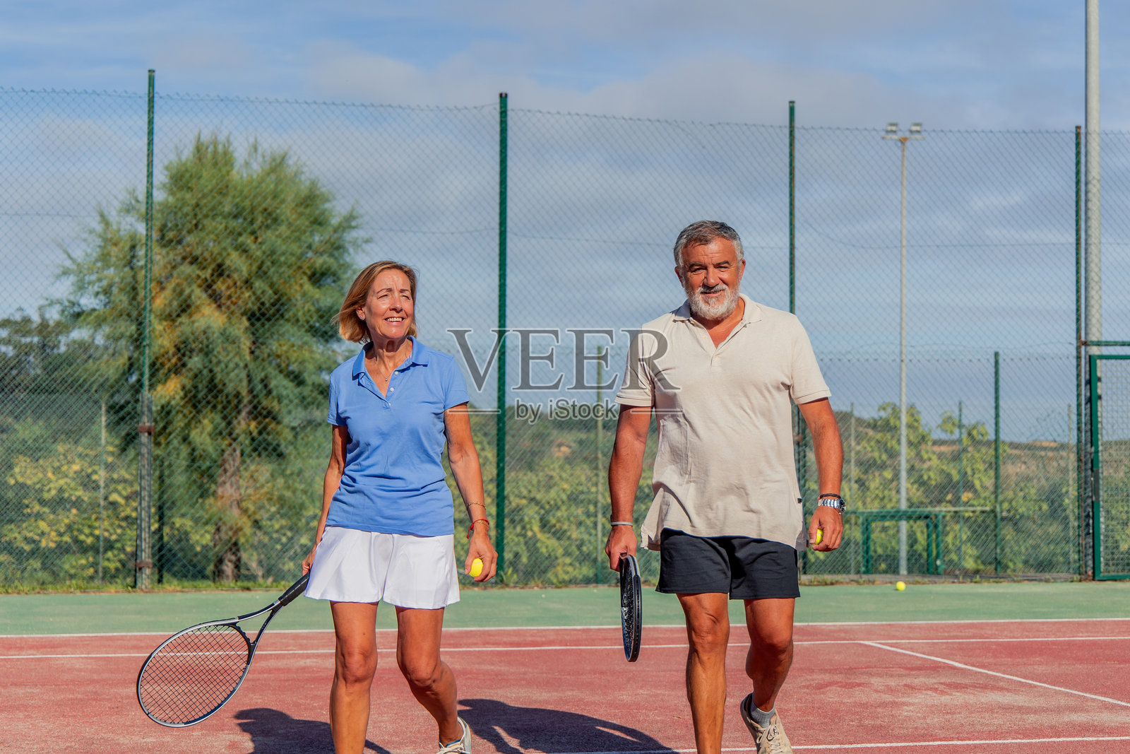 一对老年夫妇朝着镜头走去，前往网球场准备开始比赛。照片摄影图片