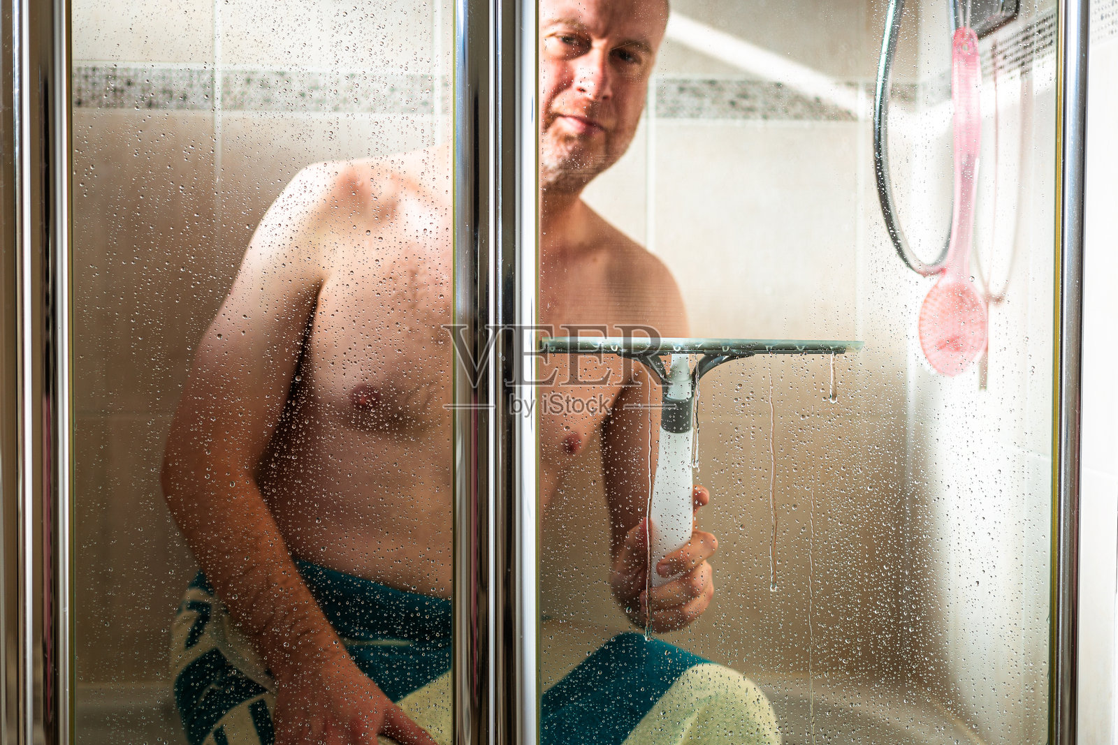 男子使用刮水器清洁淋浴玻璃面板照片摄影图片