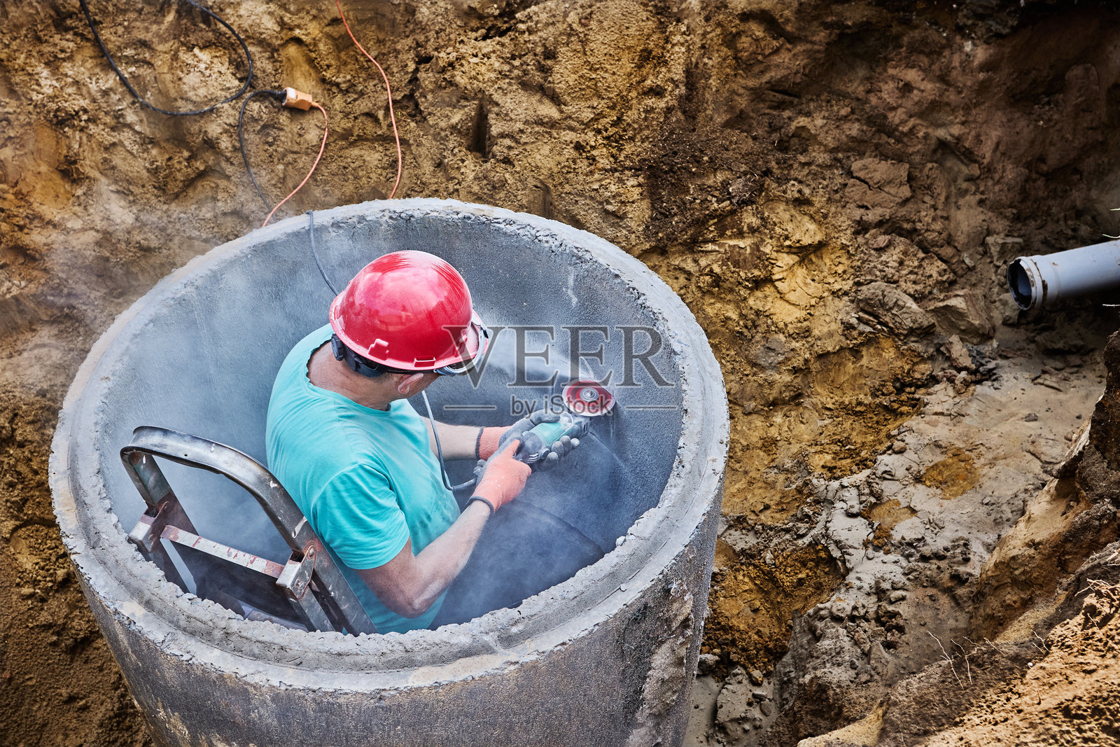使用角磨机上的金刚石切割轮在混凝土化粪池环上切割排水管孔。照片摄影图片