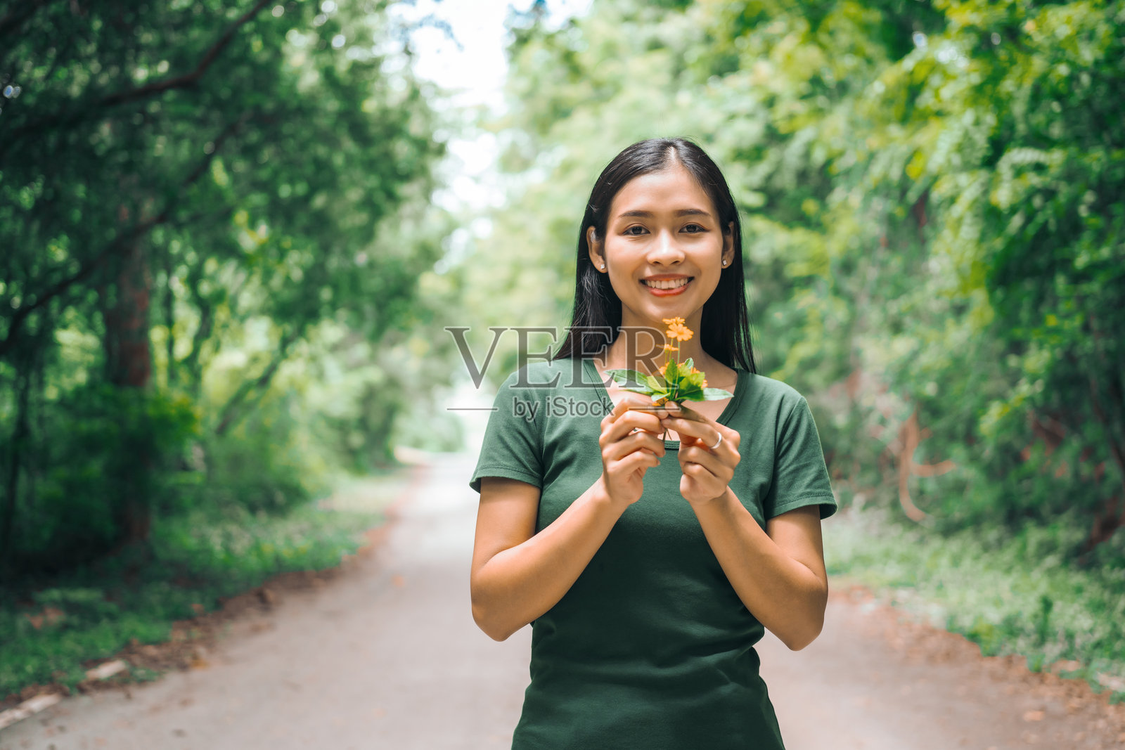 一位亚洲女性在绿色森林花园中愉快地放松，闻着花香，享受着新鲜空气。她深吸一口气，仰望早晨的阳光，感受到与大自然的和谐。照片摄影图片