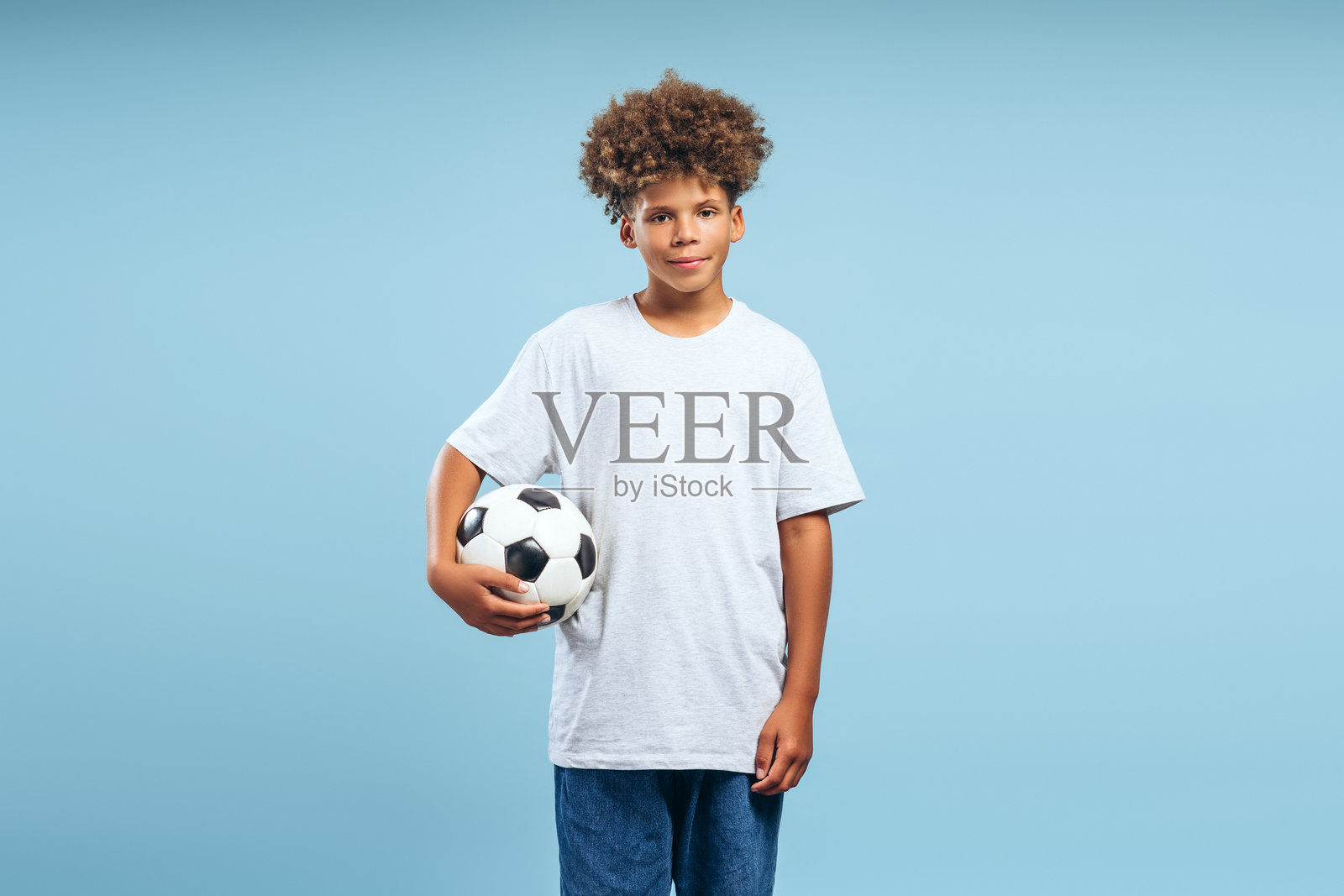 快乐的青少年，非裔美国男孩，穿着蓝色T恤的足球运动员，手里拿着足球照片摄影图片