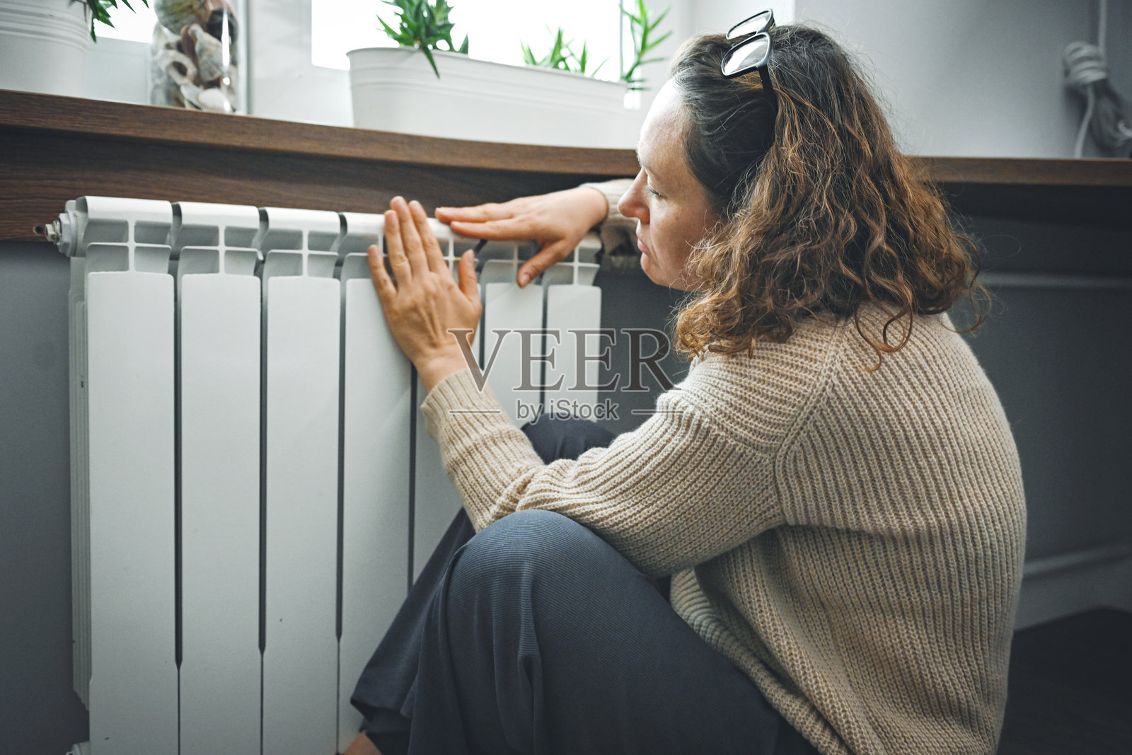 坐在窗边靠近暖气片的伤心女人照片摄影图片