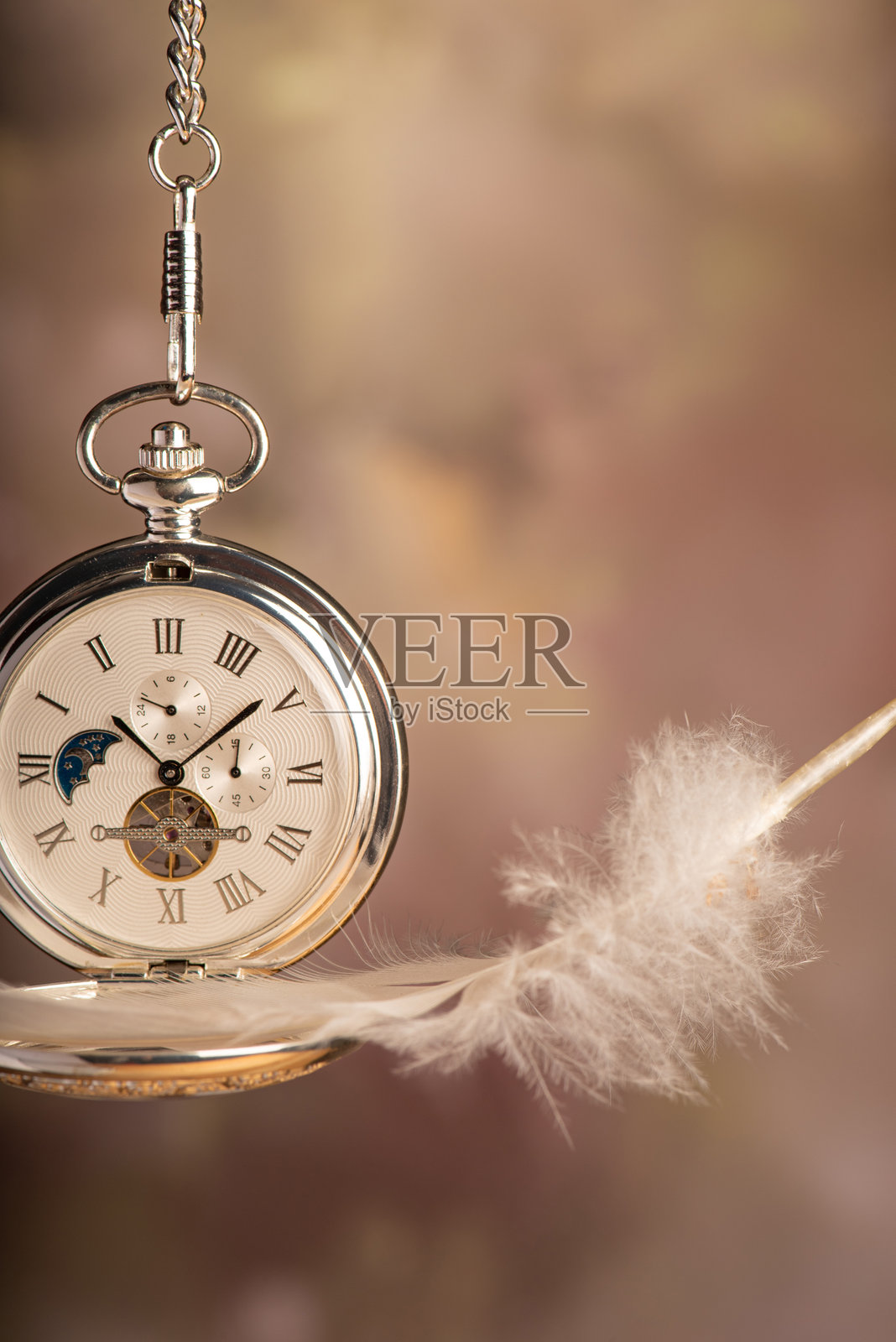 美丽的怀表和一根羽毛，悬挂在链子上，抽象背景，选择性对焦。照片摄影图片