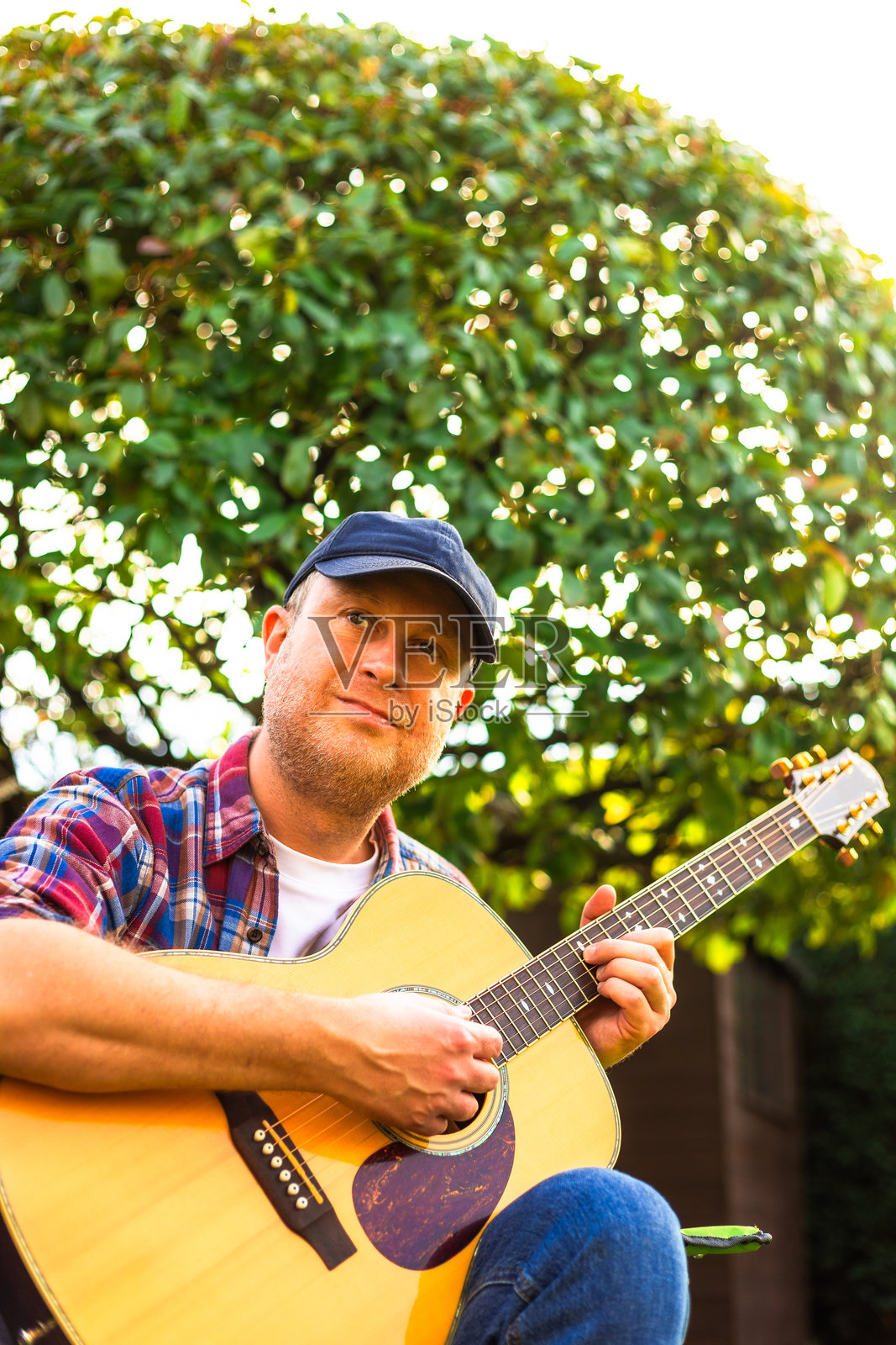 阳光明媚的日子里，满足的男人在后花园里弹奏木吉他照片摄影图片