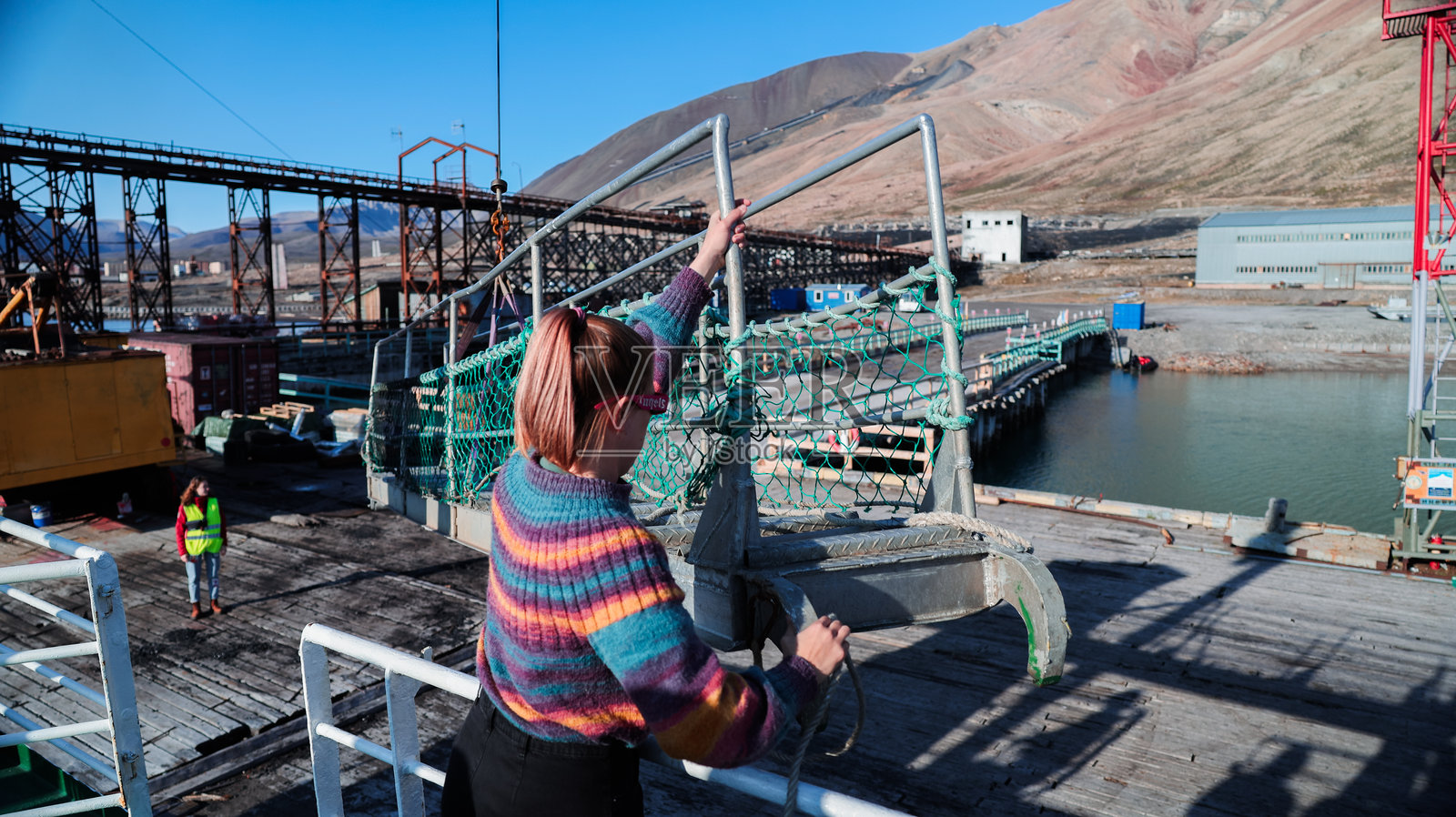 在斯瓦尔巴特港口,女性正在操作机械,背景是山脉和机械设备。照片摄影图片