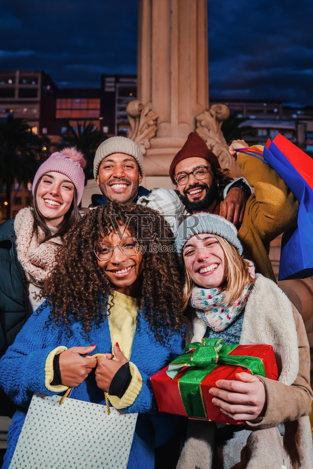 一群朋友手拿购物袋和圣诞礼物，微笑着看向镜头的竖版肖像。快乐的伙伴们在庆祝圣诞节。年轻人们享受着圣诞夜。照片摄影图片