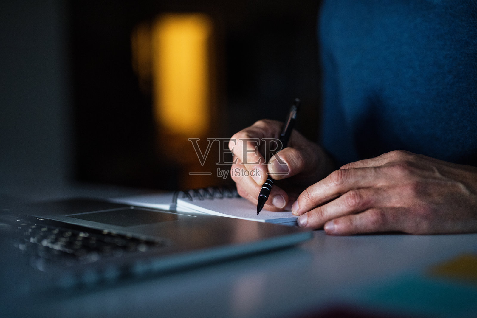 晚上在家办公的男人特写，正在计划本上写笔记。远程办公与家庭办公室。照片摄影图片