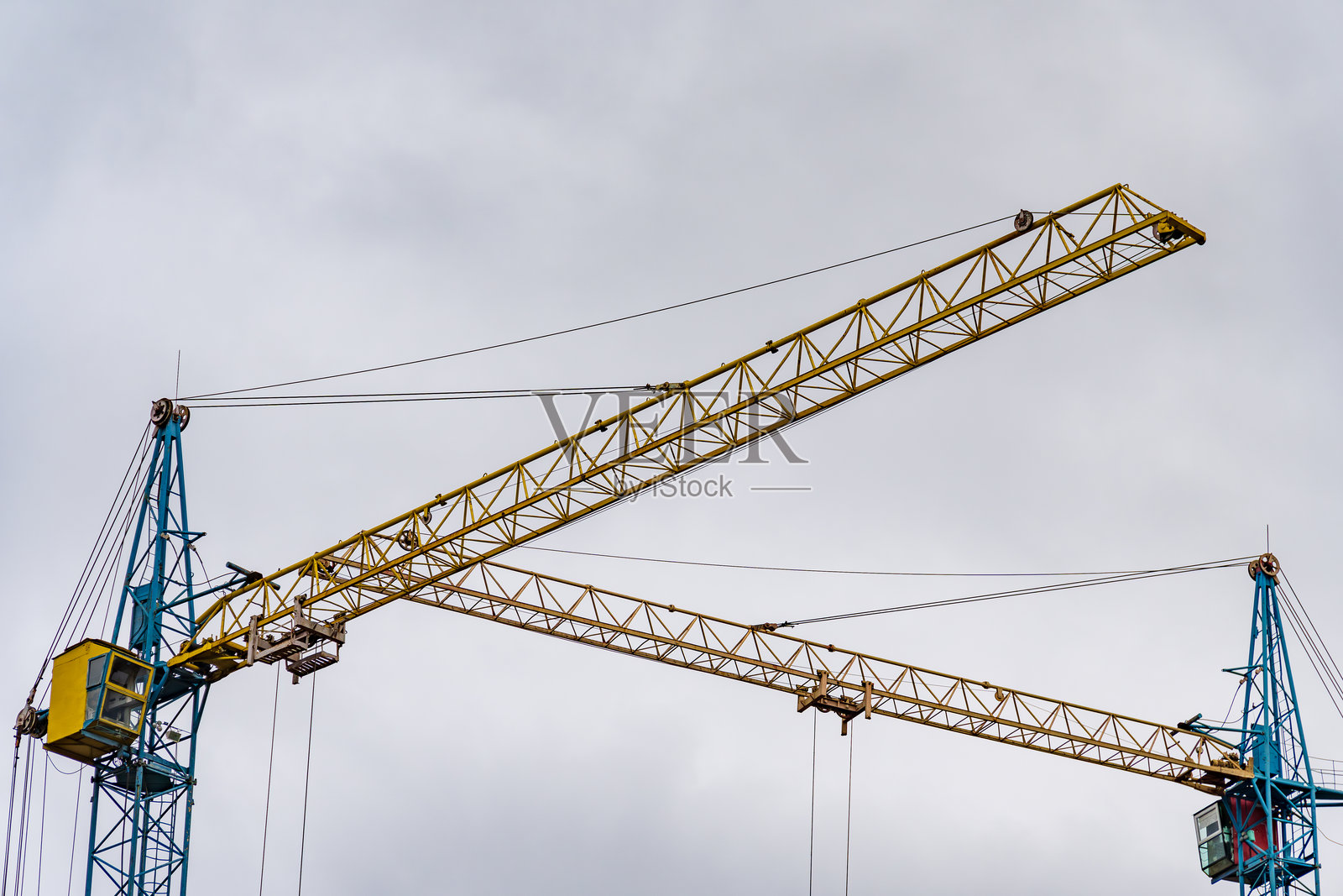 巨大的建筑起重机向阴云密布的天空伸展，展示出其复杂的结构。它们在塑造不断发展的城市景观中发挥着关键作用，突显了工业进步。照片摄影图片