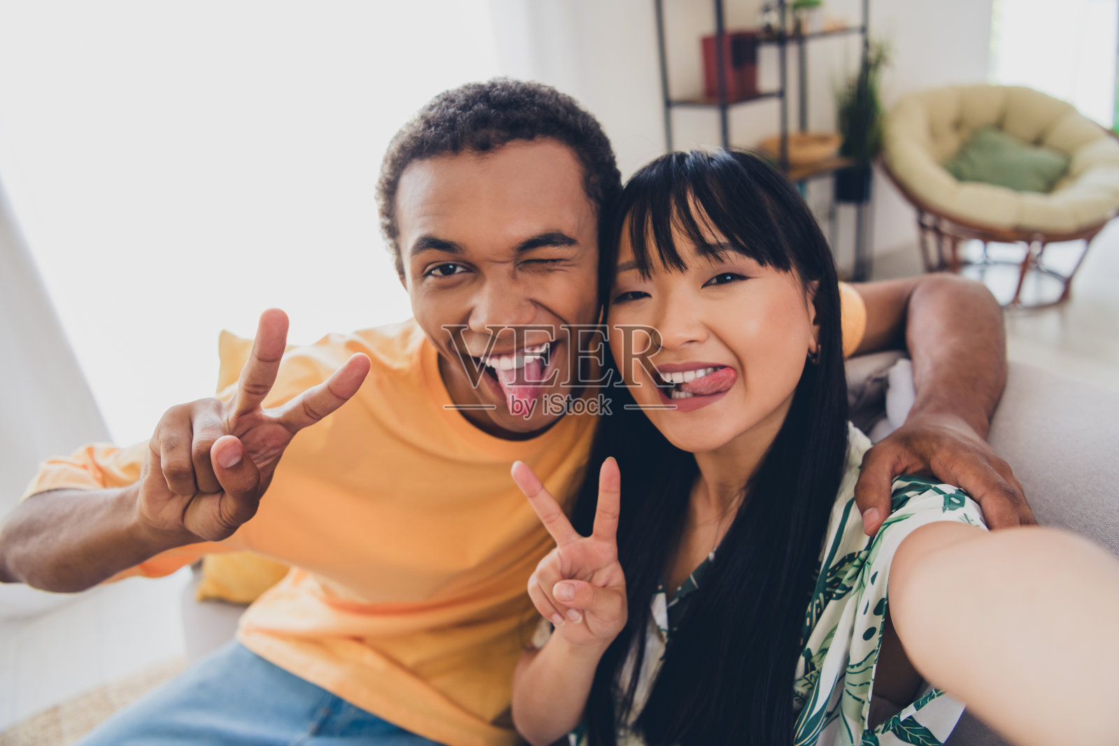 快乐无忧的积极情侣在室内公寓享受共度时光，做出V字手势照片摄影图片