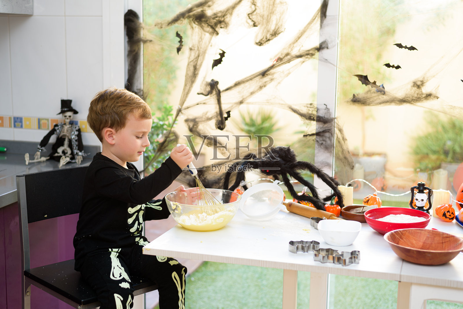 孩子在厨房里穿着骷髅服装搅拌万圣节饼干的材料照片摄影图片