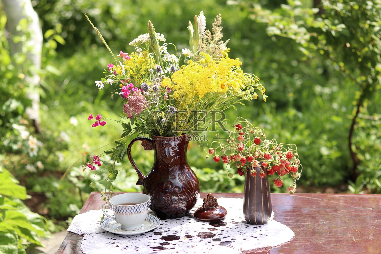 花园桌子上的陶土花瓶，里面插着野花，旁边还有一个装有草莓的花瓶照片摄影图片