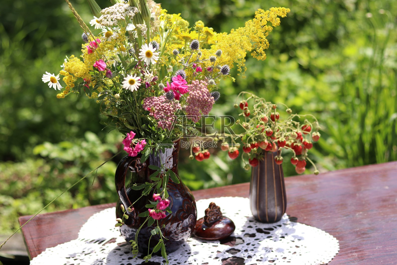 花园桌子上的陶土花瓶，里面插着野花，旁边还有一个装有草莓的花瓶照片摄影图片