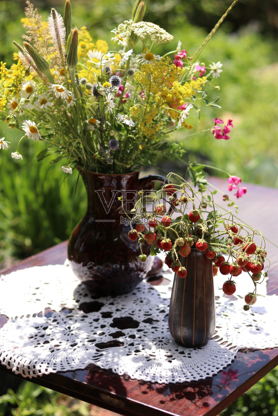 花园桌子上的陶土花瓶，里面插着野花，旁边还有一个装有草莓的花瓶照片摄影图片