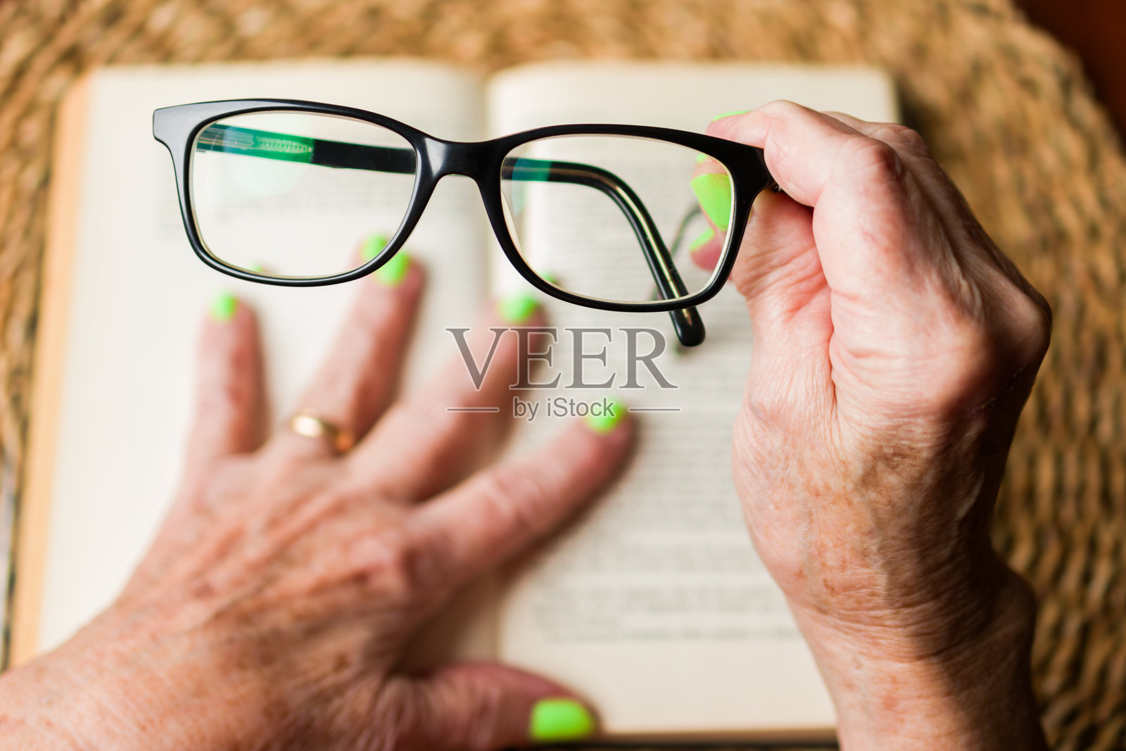 一位老妇人的手持着一副角框眼镜，解决视力问题并阅读一本书的视角。照片摄影图片