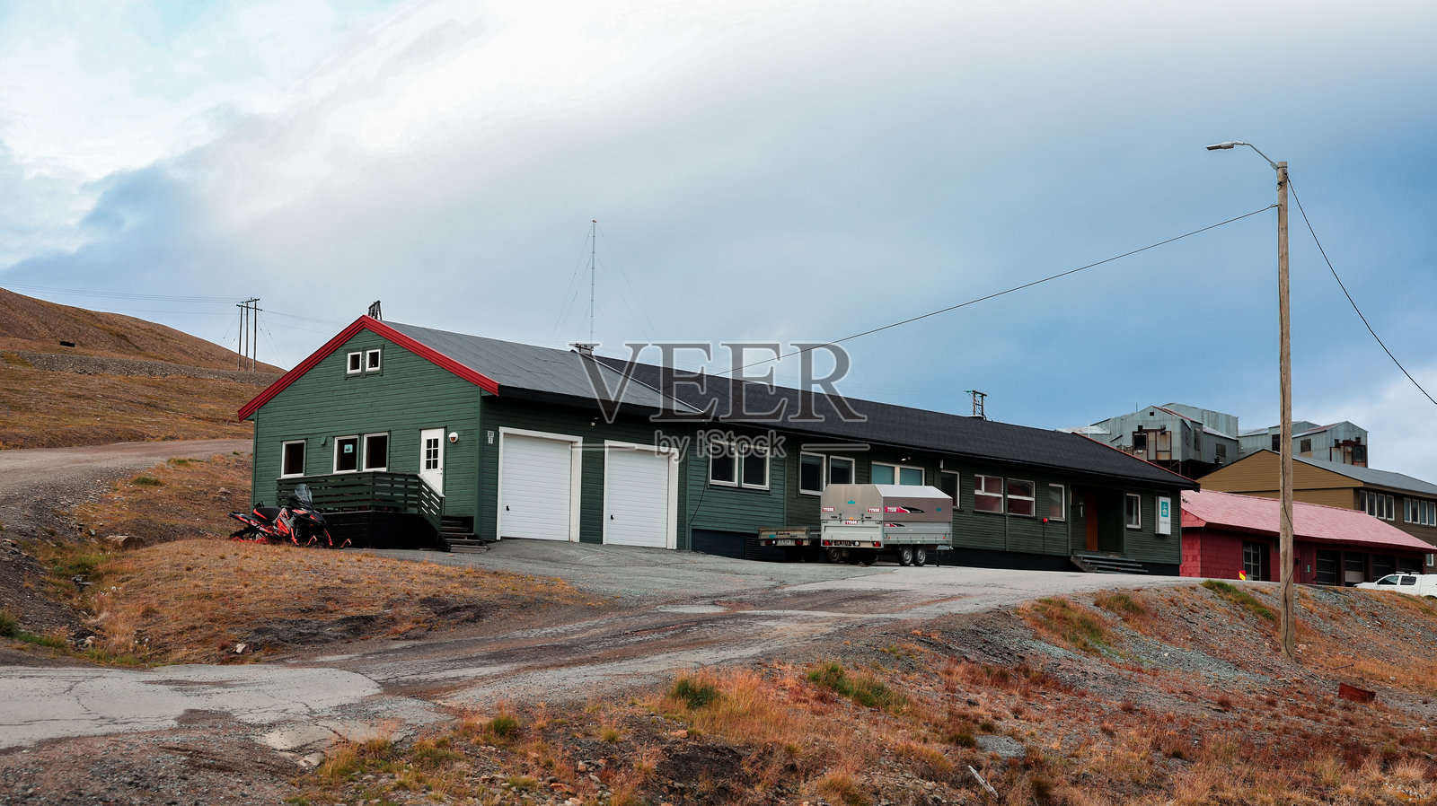 在斯瓦尔巴群岛的朗伊尔城，阴云密布的天气中，山坡路上的绿色木建筑照片摄影图片
