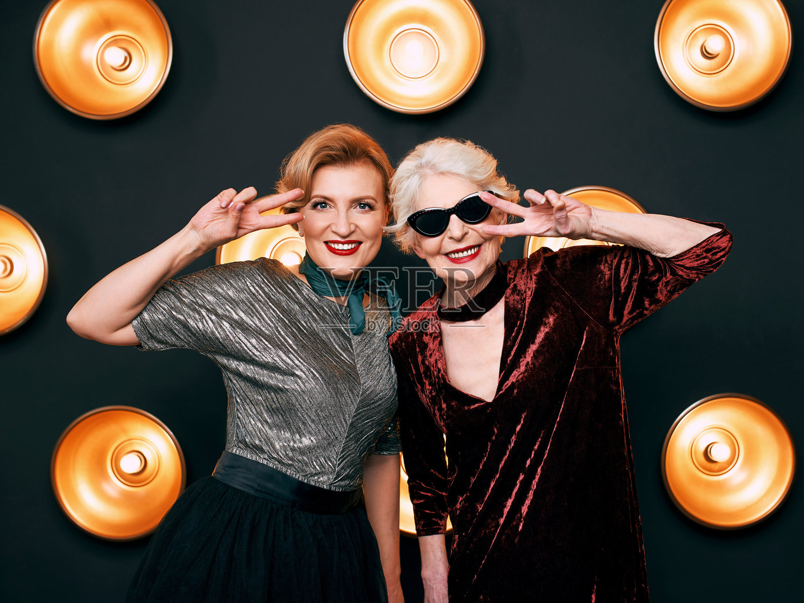 时尚优雅的老年女性与朋友在昏暗背景下佩戴太阳镜。派对、时尚、庆祝、抗衰老概念照片摄影图片