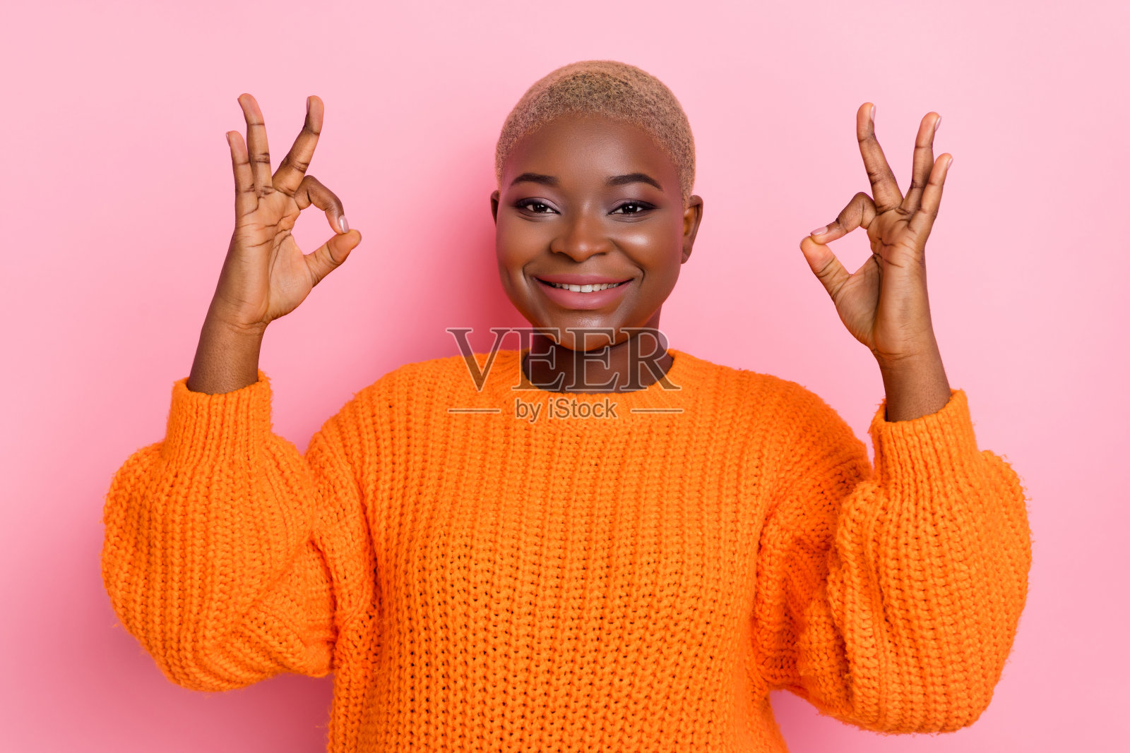 积极迷人的女士肖像，手指做出“好”的手势，背景为粉色。照片摄影图片