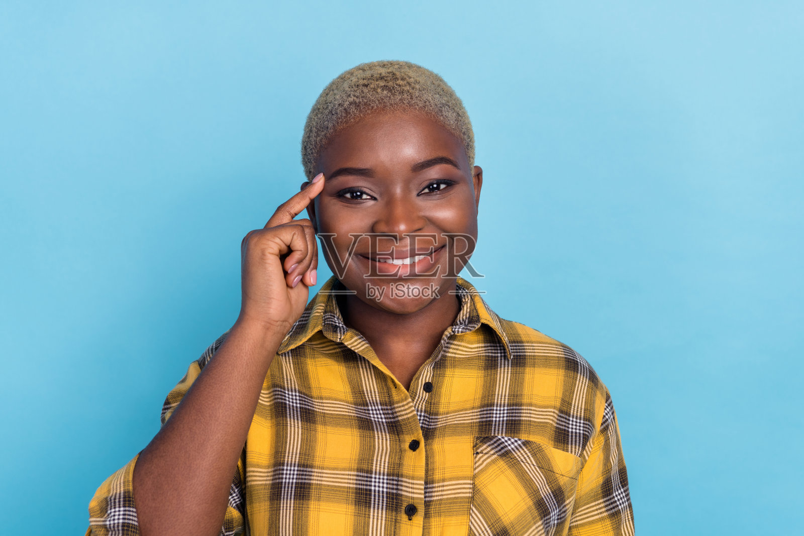 可爱的聪明女性穿着格子衬衫，微笑着用手指轻触太阳穴，背景为蓝色。照片摄影图片