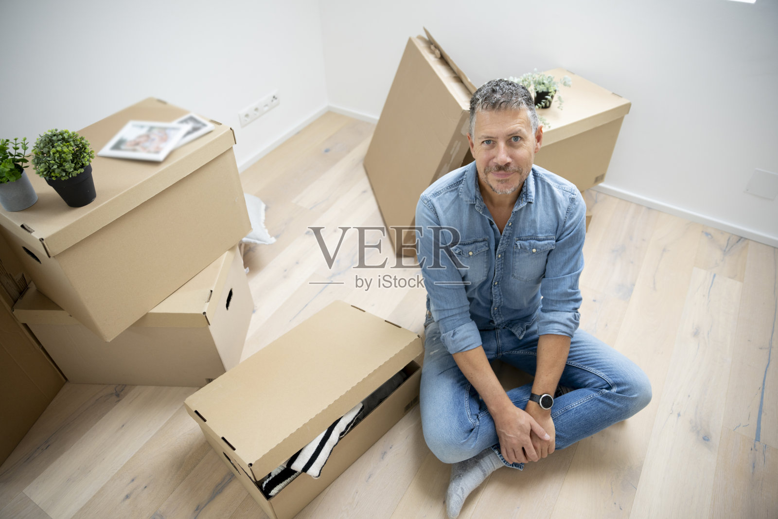 中年男子坐在新公寓的地板上，周围是搬家的箱子。照片摄影图片