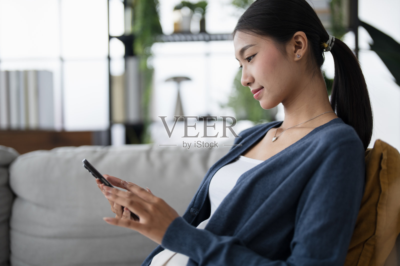 亚洲女性在家沙发上使用智能手机，沉迷于社交媒体，享受手机科技带来的社交成瘾。照片摄影图片