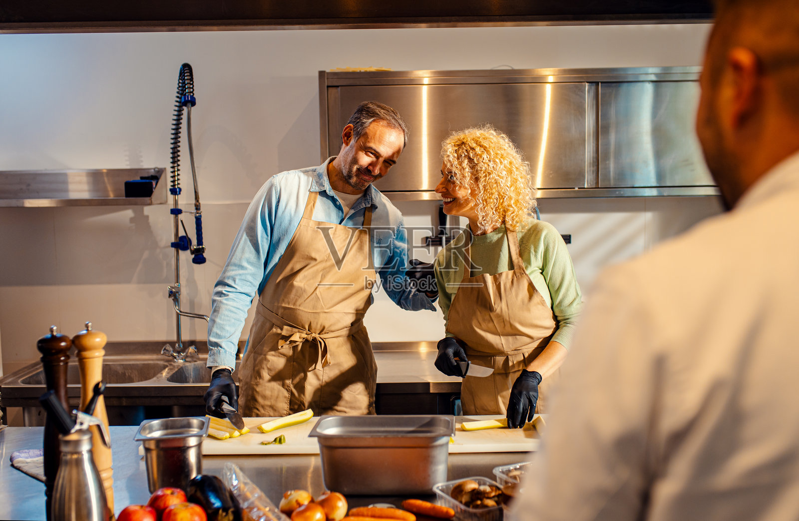 中年夫妇在厨房里参加烹饪课程，和厨师一起准备餐点用的西葫芦。照片摄影图片