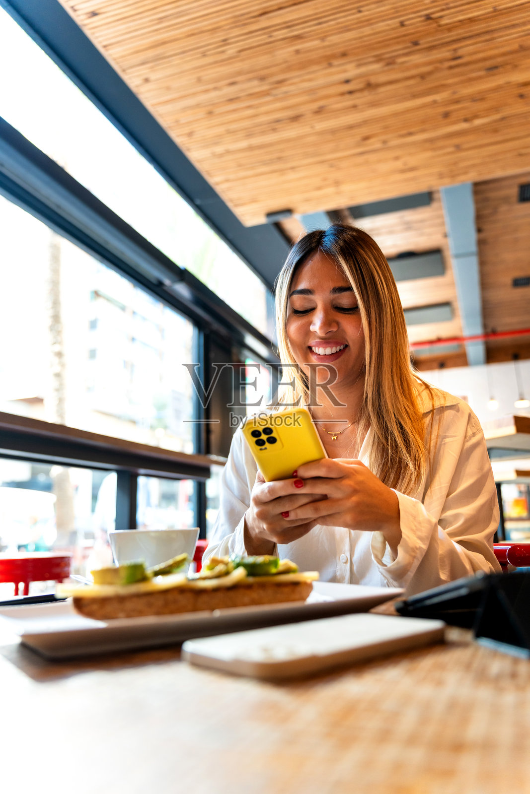 自信的拉丁裔女商人在早餐时 juggling 手机并进行多任务处理照片摄影图片