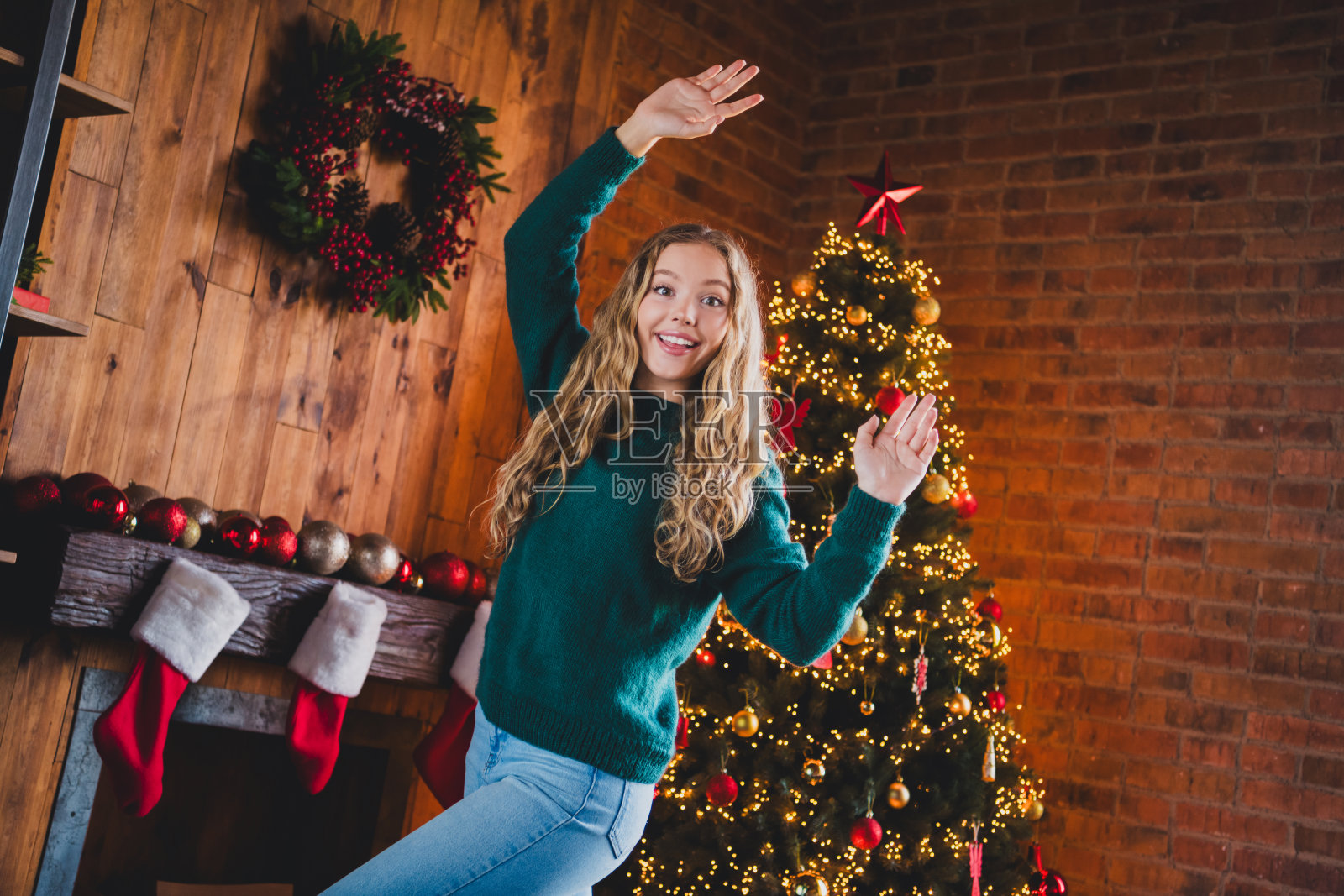 穿着绿色圣诞服装的可爱少女在室内现代舒适的圣诞派对装饰环境中跳舞，享受快乐时光。照片摄影图片