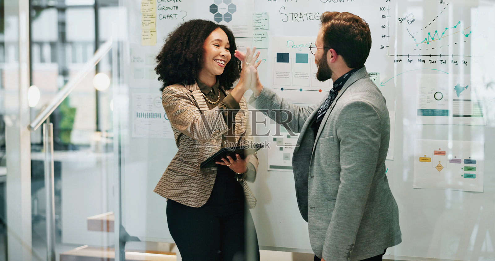 商务人士在办公室用白板进行高兴的击掌，象征团结或庆祝，作为趋势分析师。员工、合作伙伴微笑，展现团队合作、协作和战略的协同效应。照片摄影图片