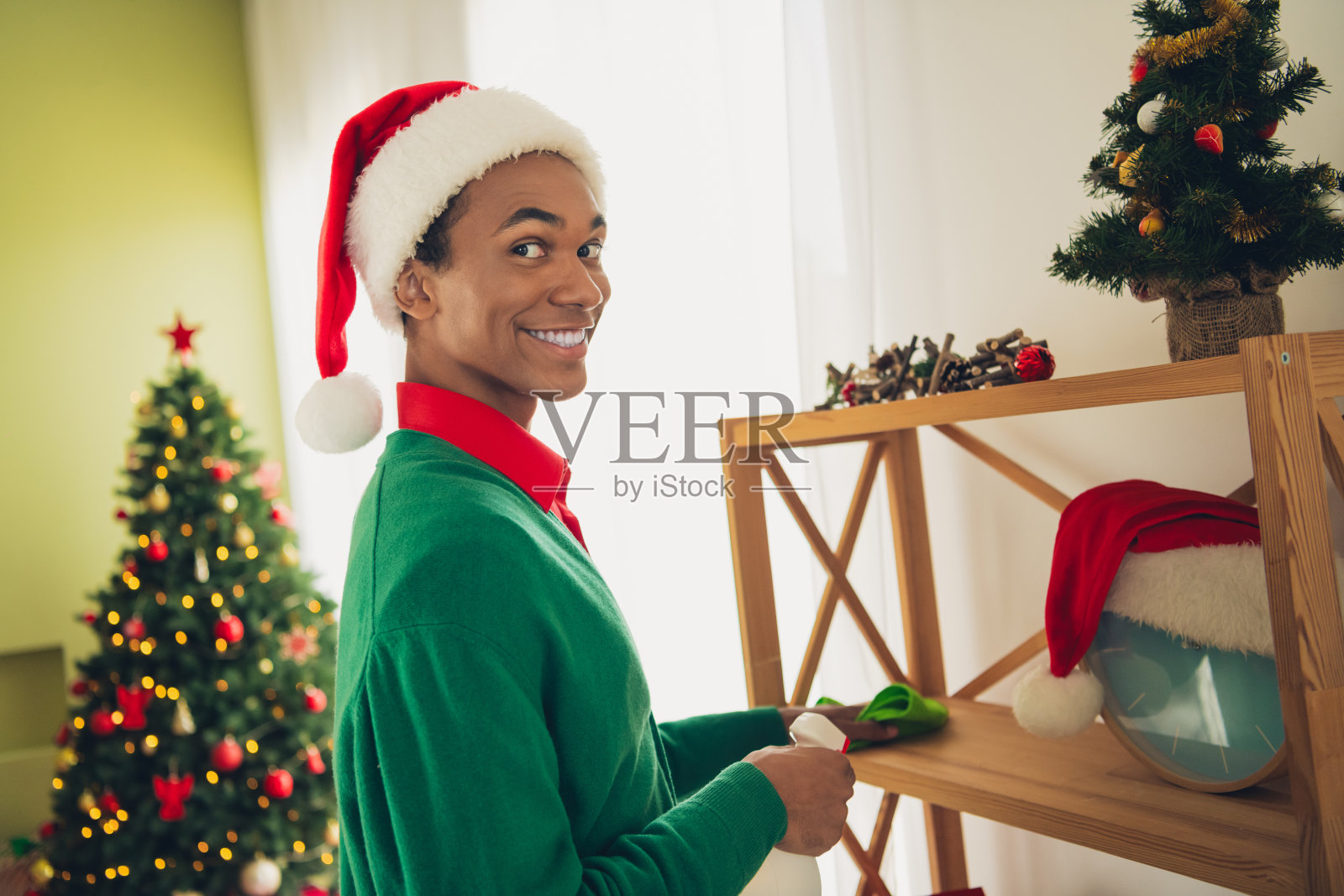 穿着绿色毛衣的帅气男士在室内打扫卫生，庆祝圣诞节。照片摄影图片