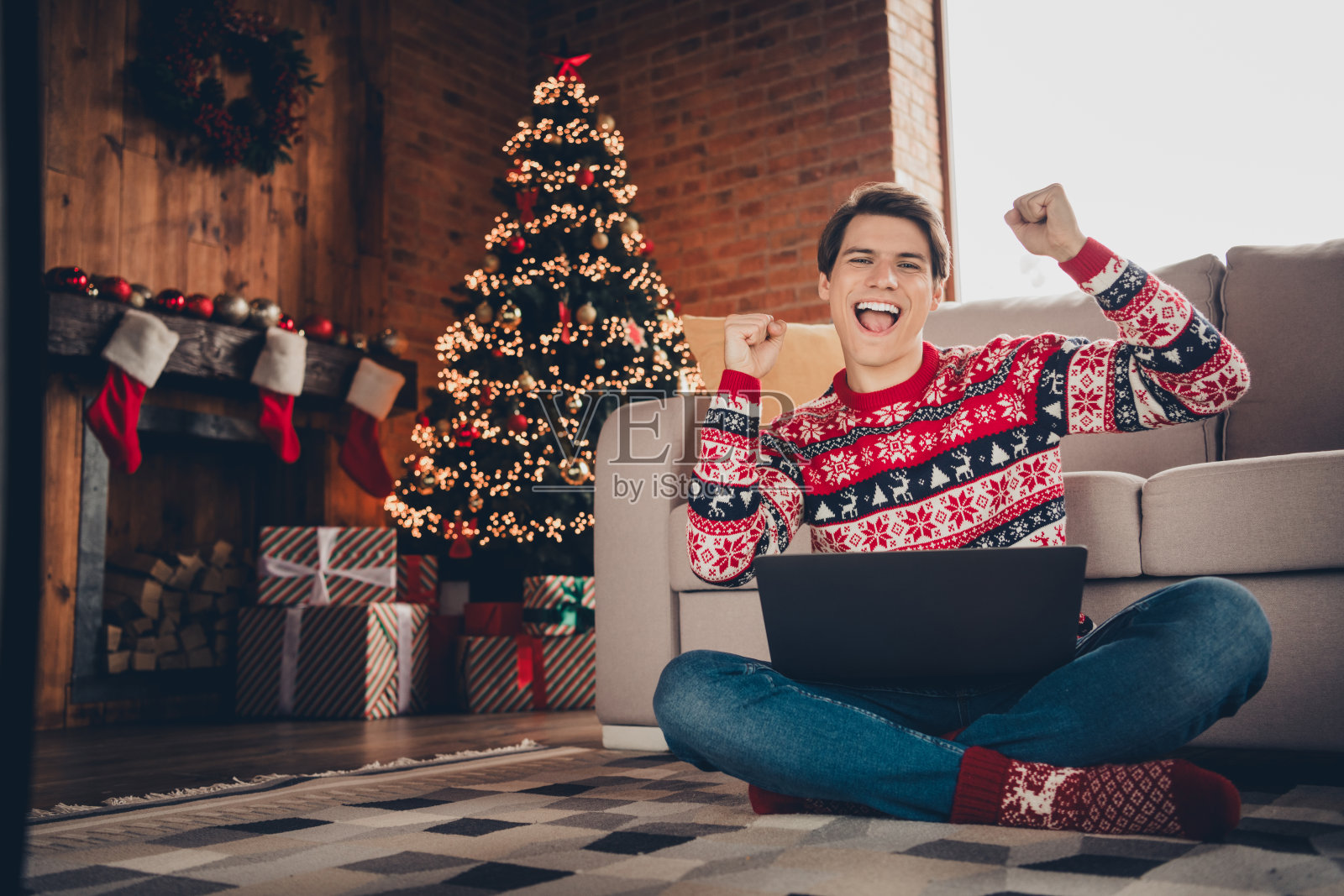 穿着花哨毛衣的幸运小伙子在室内公寓里享受圣诞节，玩现代电子设备，心情愉快。照片摄影图片