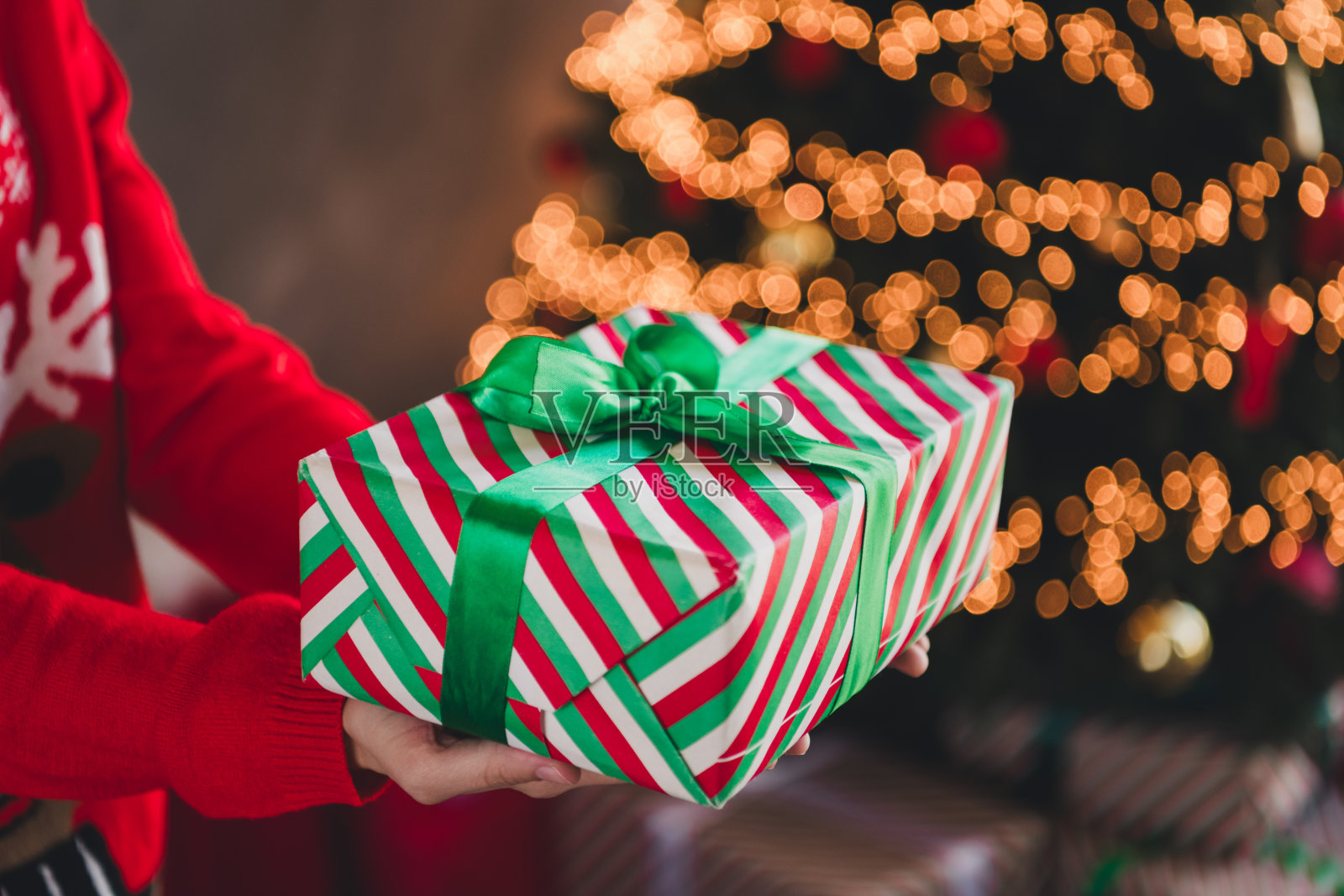 年轻女性穿着圣诞服装，手持礼品盒，房间内装饰着传统的节日气氛。照片摄影图片