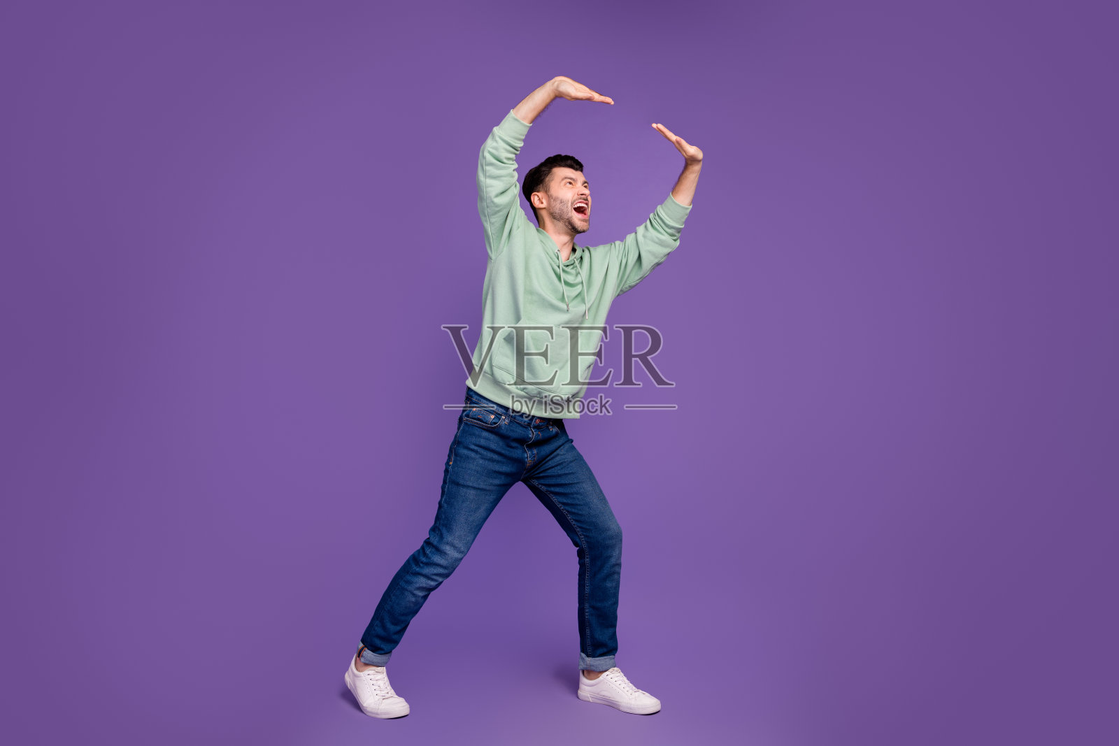 全身照，英俊的年轻男子穿着时尚的卡其色服装，举起沉重的墙面购物横幅，背景为紫色。照片摄影图片