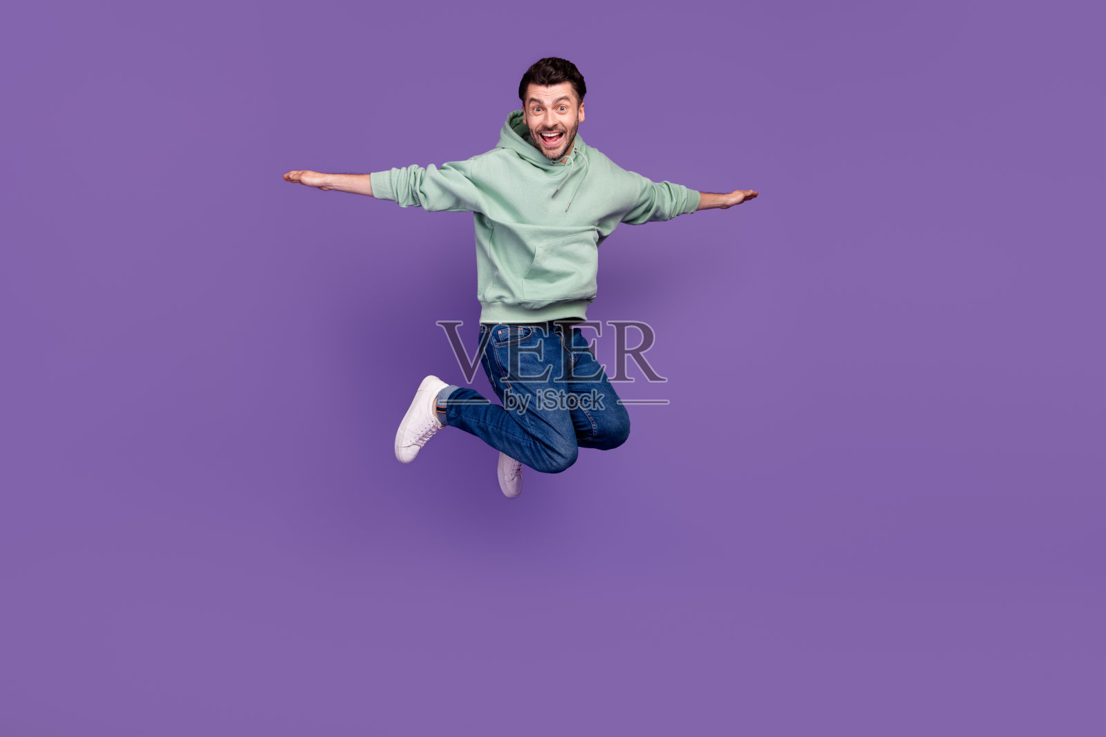 充满活力的快乐男人在紫色背景上跳跃，双臂张开像翅膀一样飞翔的全身照片照片摄影图片