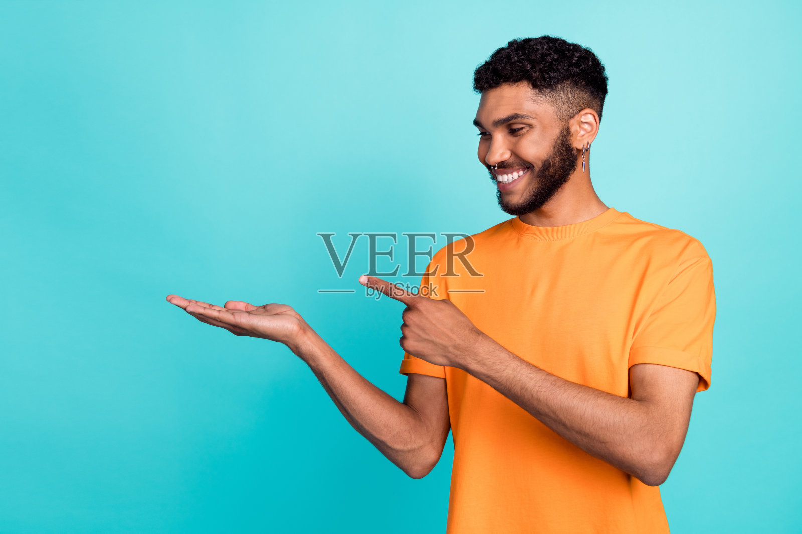 梦幻甜美的男子穿着橙色T恤，手指指向空白处，背景为青绿色。照片摄影图片