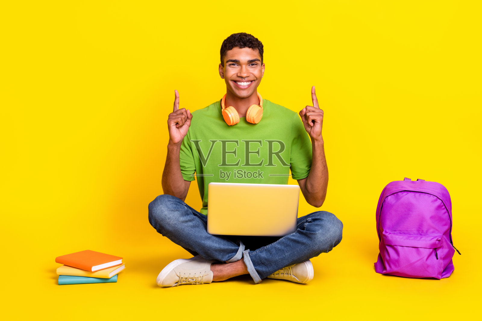 全身照，快乐搞笑的男士穿着绿色T恤，手持现代小工具，指向空白空间，背景为黄色。照片摄影图片