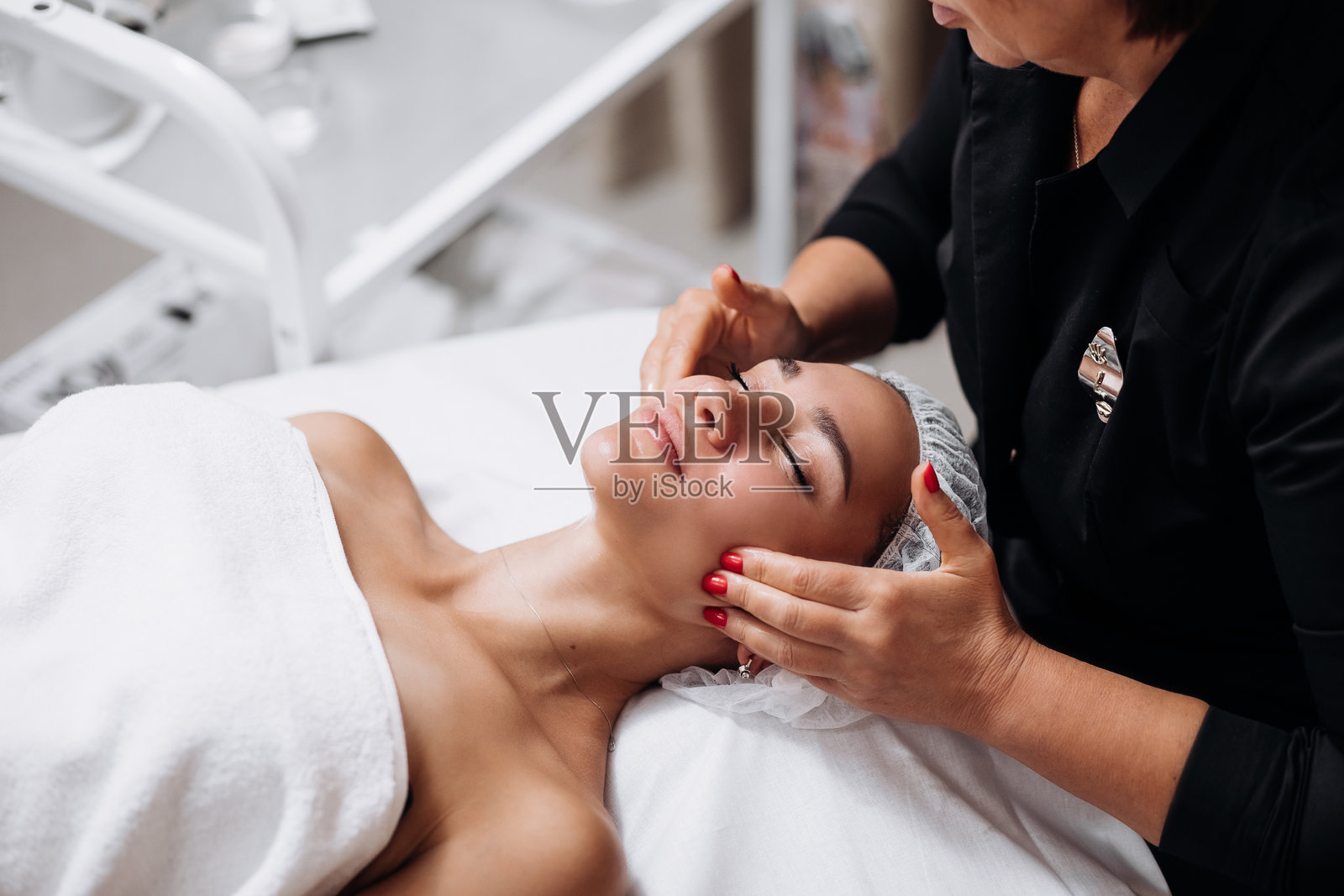 美容院内，按摩师的手部特写，为年轻女性进行放松的面部按摩。这个场景突显了专业护理和水疗治疗的舒缓益处。照片摄影图片