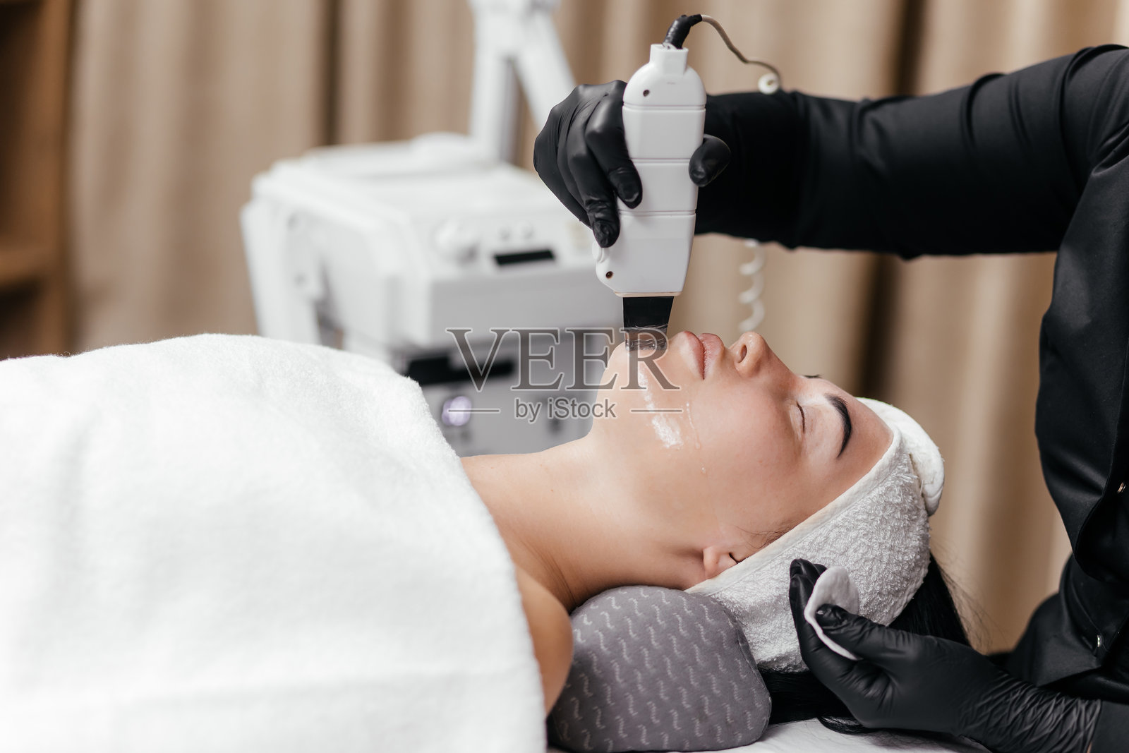 美容师使用超声波刮刀为年轻女性进行面部护理的特写镜头。场景突出了超声波面部去角质，展示了其在护肤疗法中的有效性。照片摄影图片