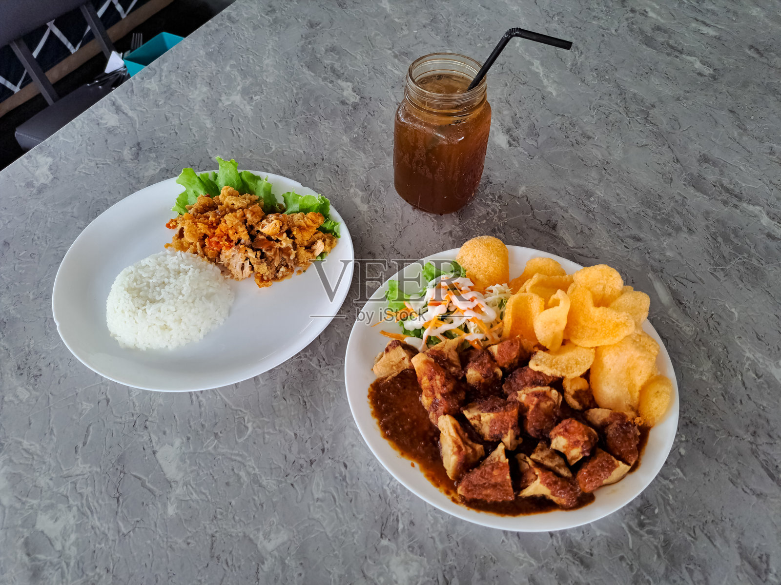 炸豆腐肉丸（Batagor）和照烧捣碎炸鸡（Nasi Ayam Geprek Teriyaki）。新鲜冰茶（Es Teh Segar）盛在玻璃杯中。食品和饮料菜单。照片摄影图片