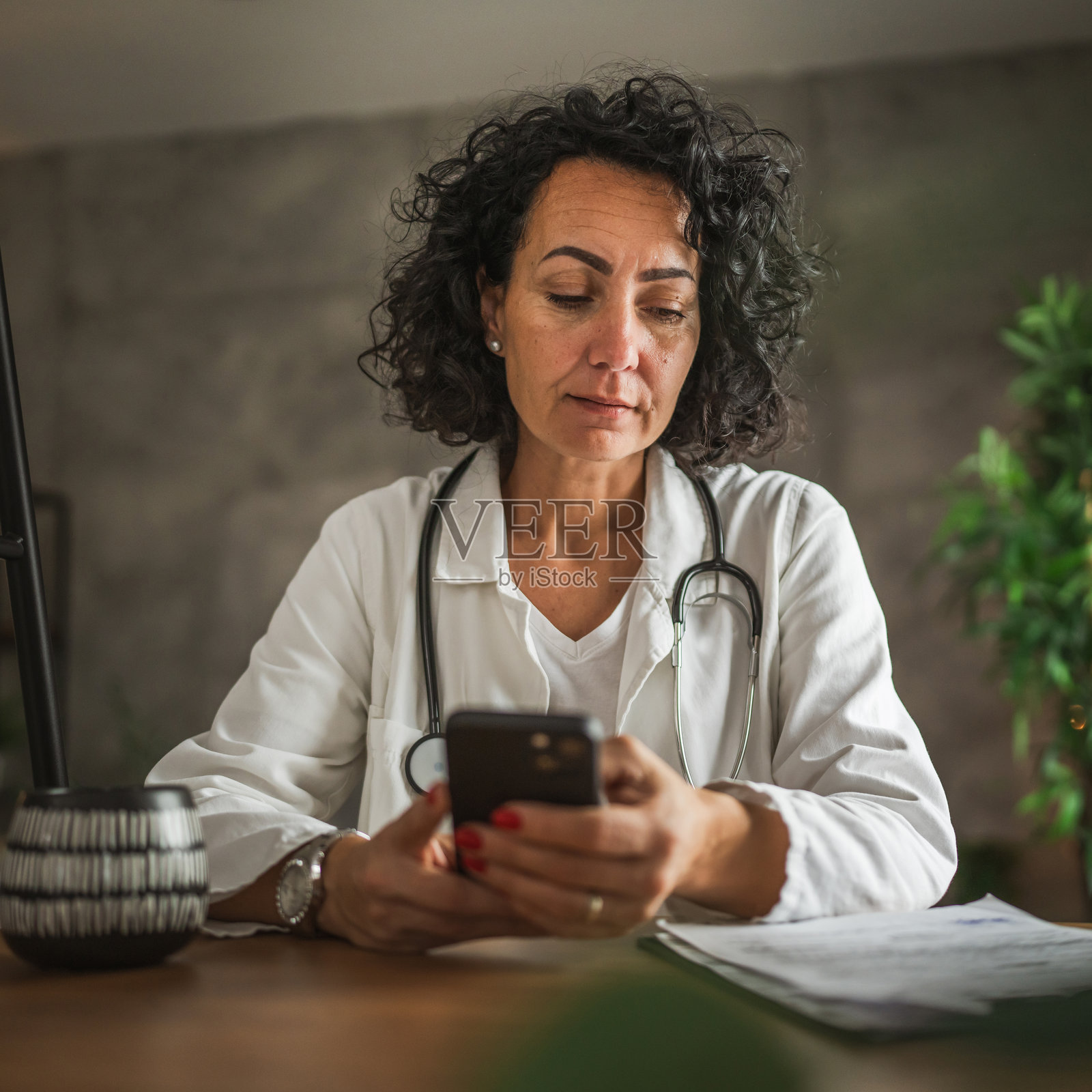 成熟的女性医生坐在家中使用手机照片摄影图片